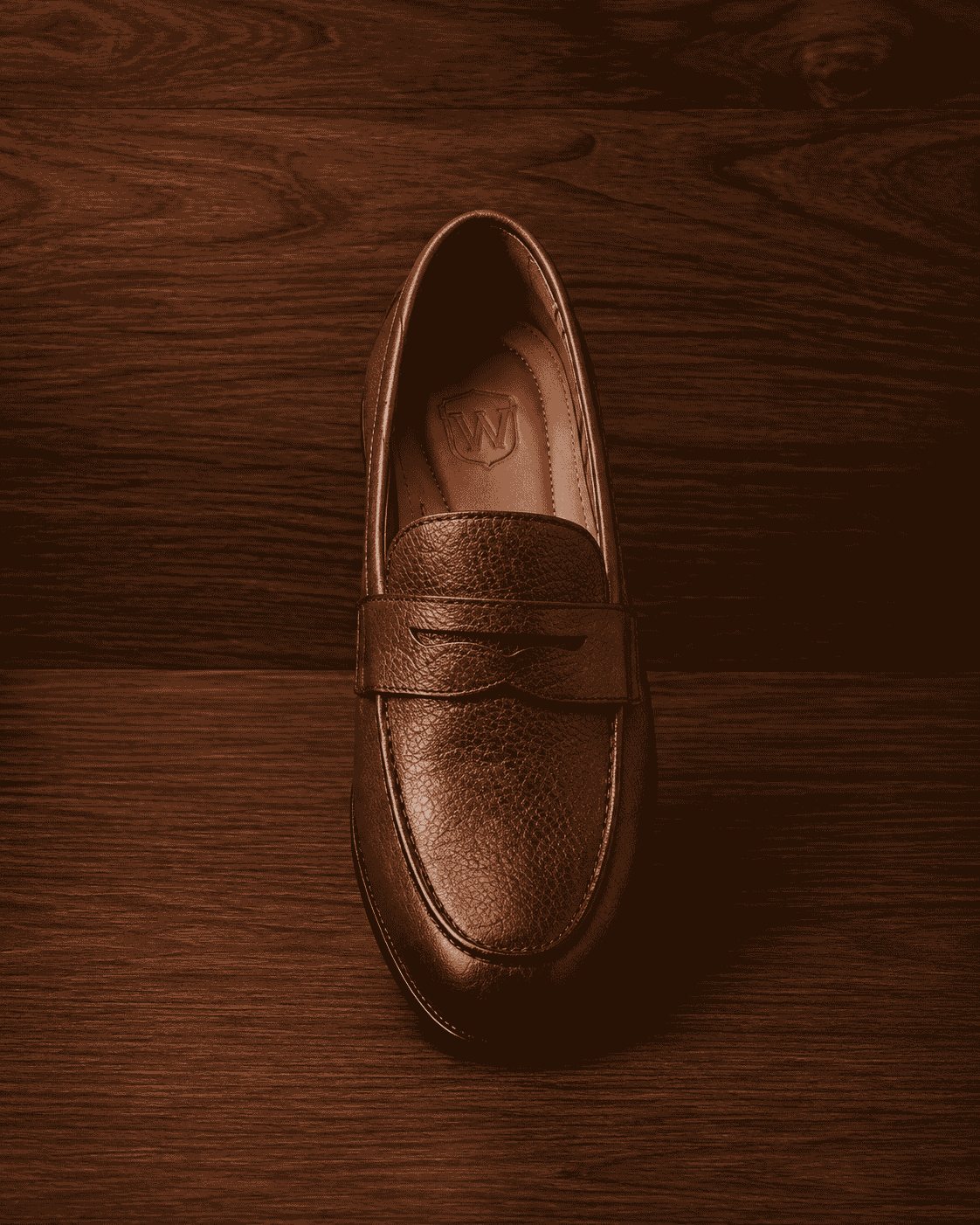 Men's brown pebbled leather penny loafer with classic strap on dark wood backdrop